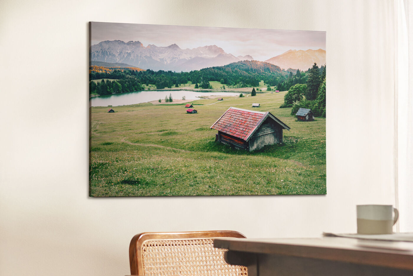 CEWE Wandbild mit ruhiger Landschaft zeigt grüne Wiese, kleines Holzhaus und Berge im warmen Abendlicht.